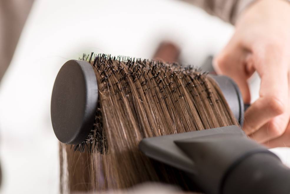 Mujer se seca el cabello con un secador y un moldeador