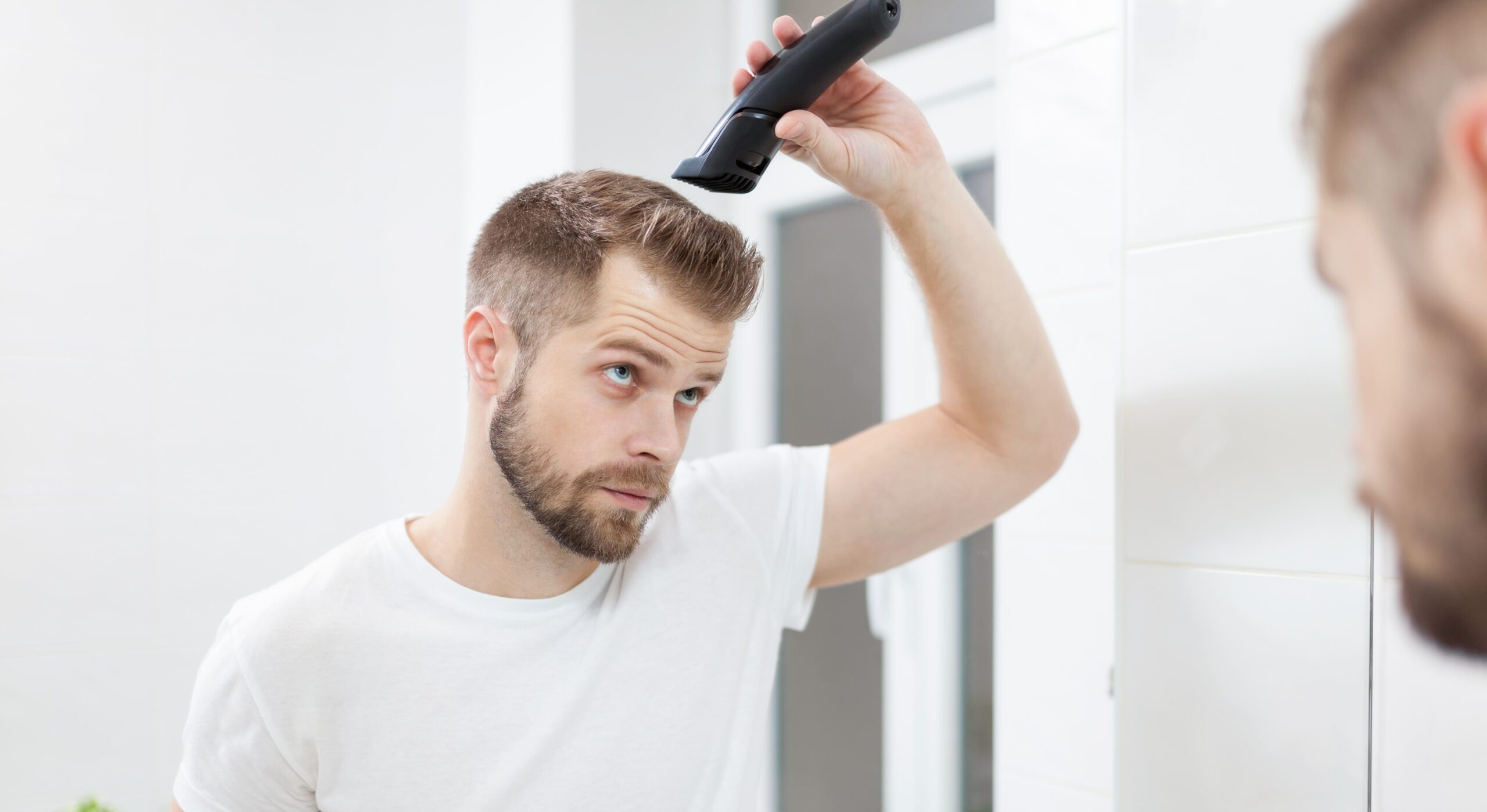 Haarkranz Frisur - gut aussehender Mann schneidet sich die Haare mit einem Haarschneider