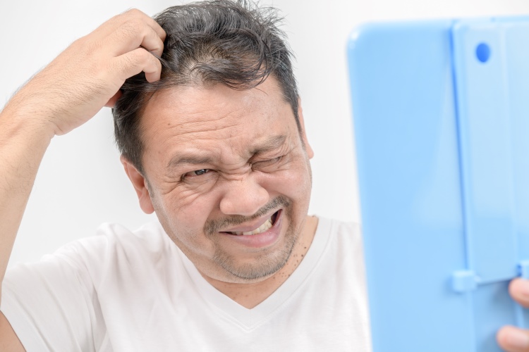 Mann schaut in sein Tablet und kratzt sich die Kopfhaut wegen Seborrhoische Dermatitis