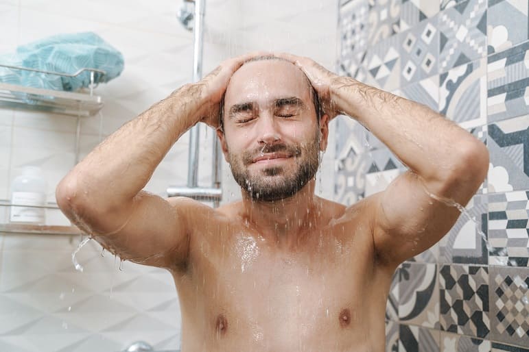 Lächender Mann beim Haare waschen unter der Dusche