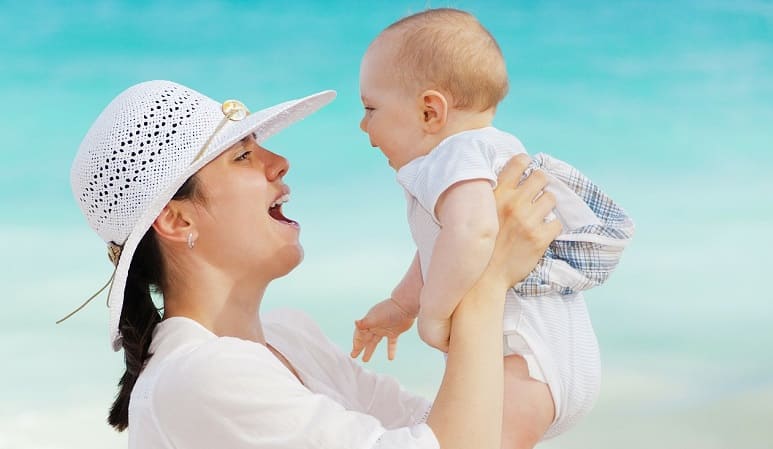 Frau mit Baby auf dem Arm freut sich, keinen Haarausfall in der Stillzeit zu haben